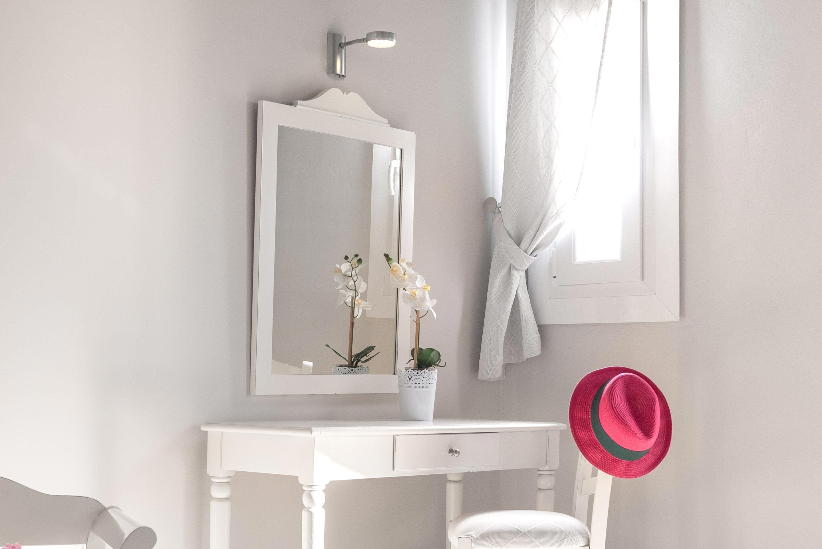 A white vanity with a mirror, a small potted plant, and a pink hat hanging on the wall.