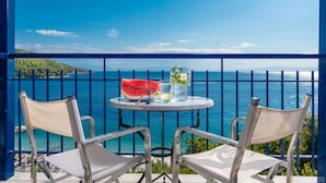Un balcon avec deux chaises en métal et une petite table ronde, d’où l’on peut admirer une mer d’un bleu limpide et une côte lointaine.