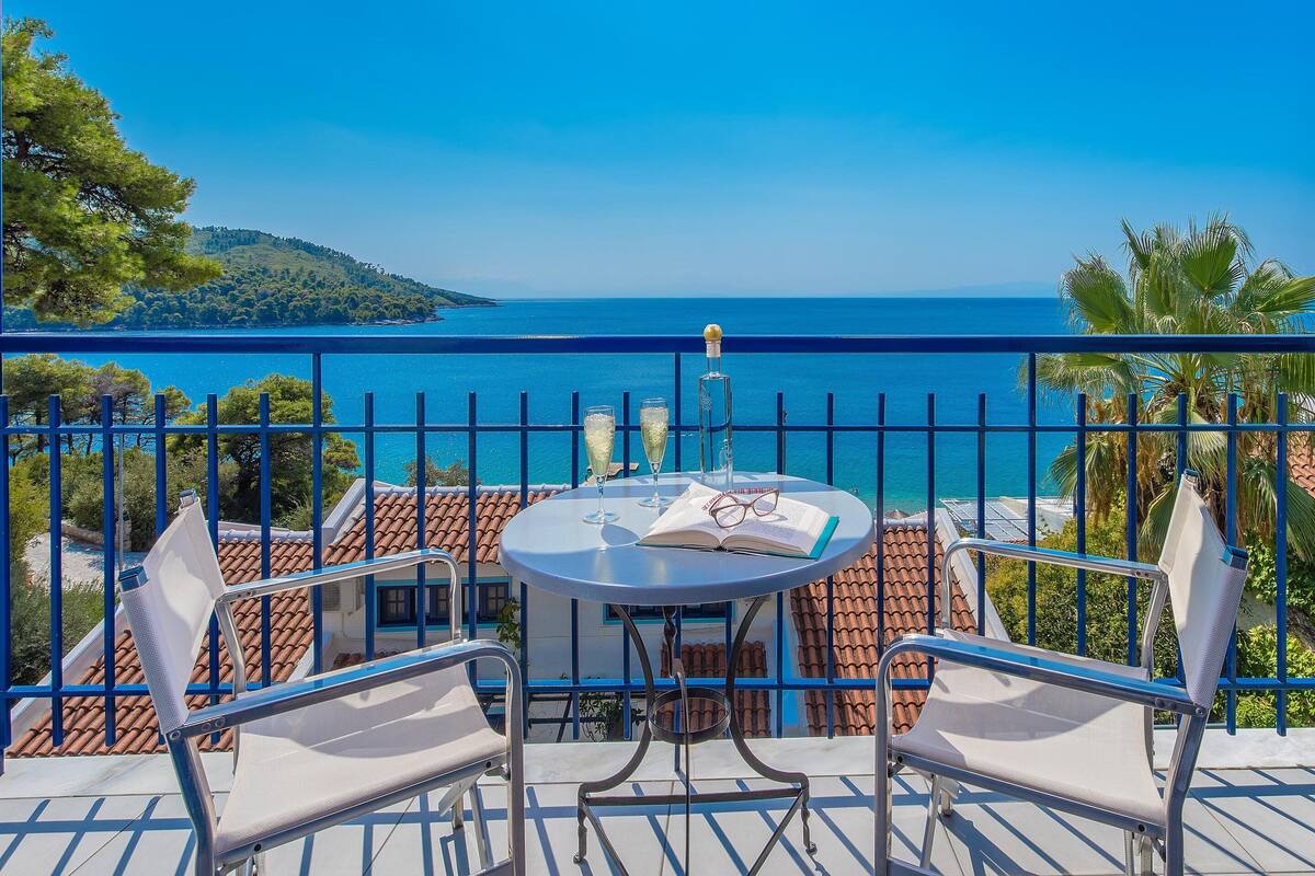 Un balcon avec une table et deux chaises, offrant une vue sur la côte et un ciel dégagé.