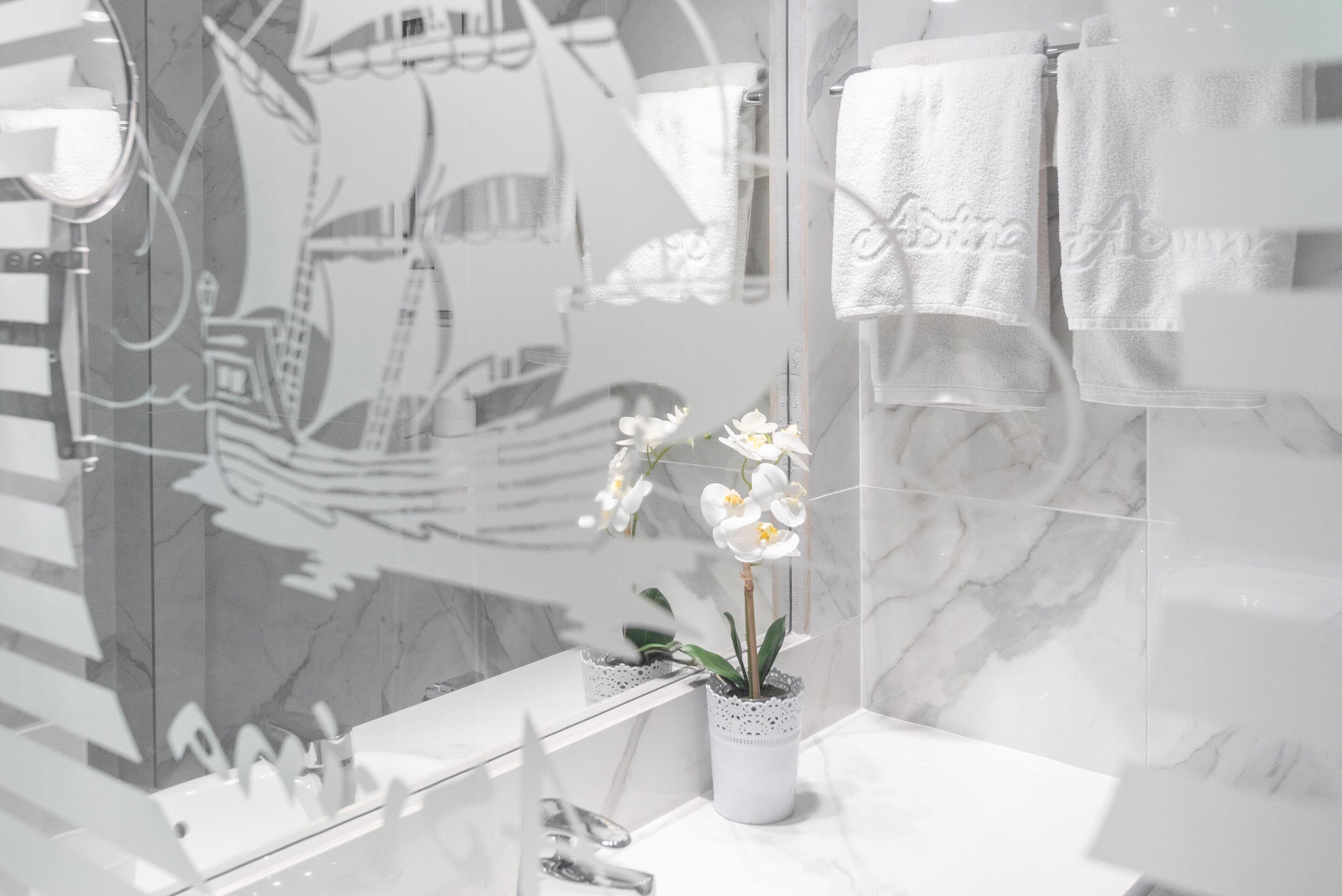 Een badkamer met een marmeren wastafel, een potorkidee en een muurschildering van een schip.