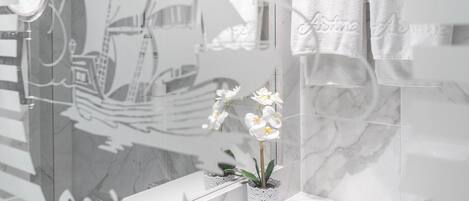 A bathroom with a marble sink, a potted orchid, and a ship mural on the wall.