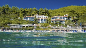 Un hôtel en bord de mer composé de plusieurs bâtiments, une plage avec des transats et une vue dégagée sur la mer.