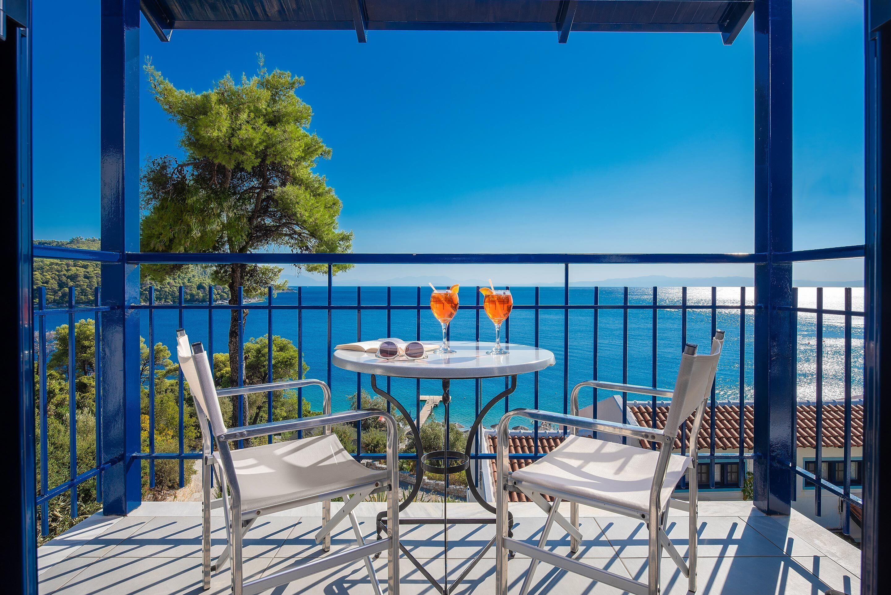 Un balcon avec une table, deux chaises et deux verres de boisson à l’orange.