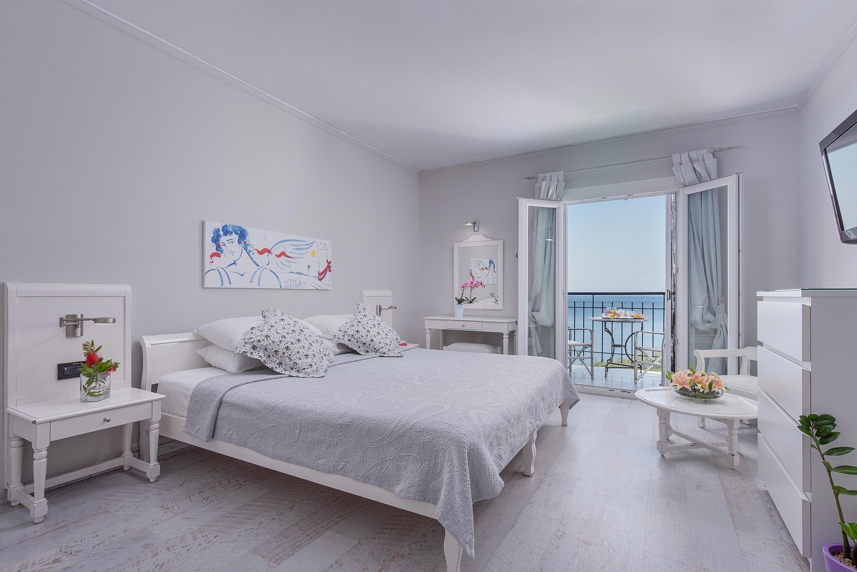 Ein Schlafzimmer mit Bett, Nachttischen, einem Fenster mit Vorhängen und einem Balkon mit Tisch und Stühlen.