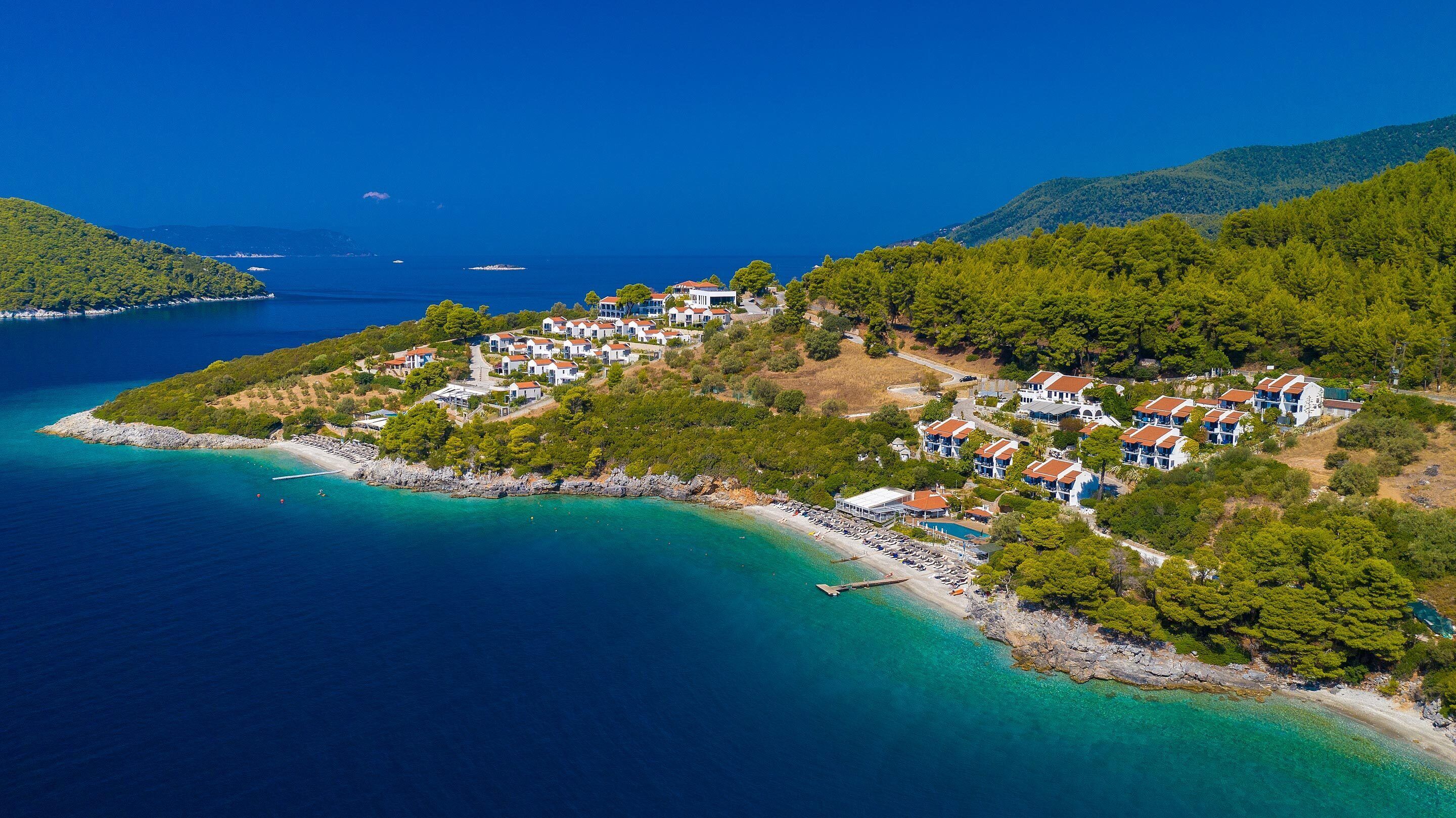 Vue aérienne d’une station balnéaire avec des villas, une plage et des eaux d’un bleu limpide.
