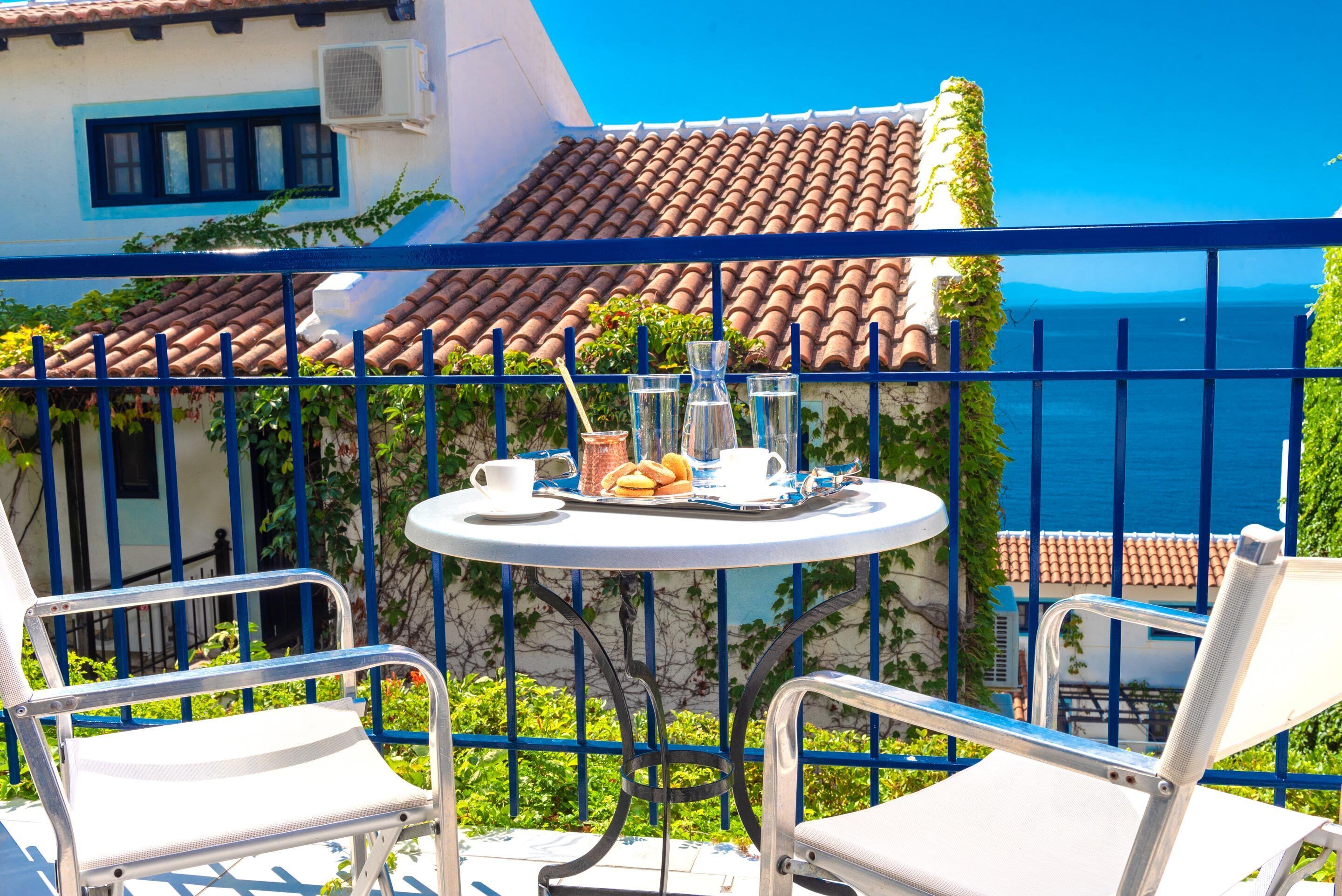 Un balcón con una mesa dispuesta para dos personas, con vistas a la costa, tejados de tejas y una vista despejada del mar.