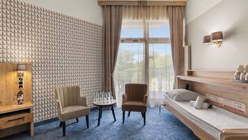 Habitación de hotel con una pared de estampado geométrico, una cama sofá, una mesita redonda con botellas y una lámpara.