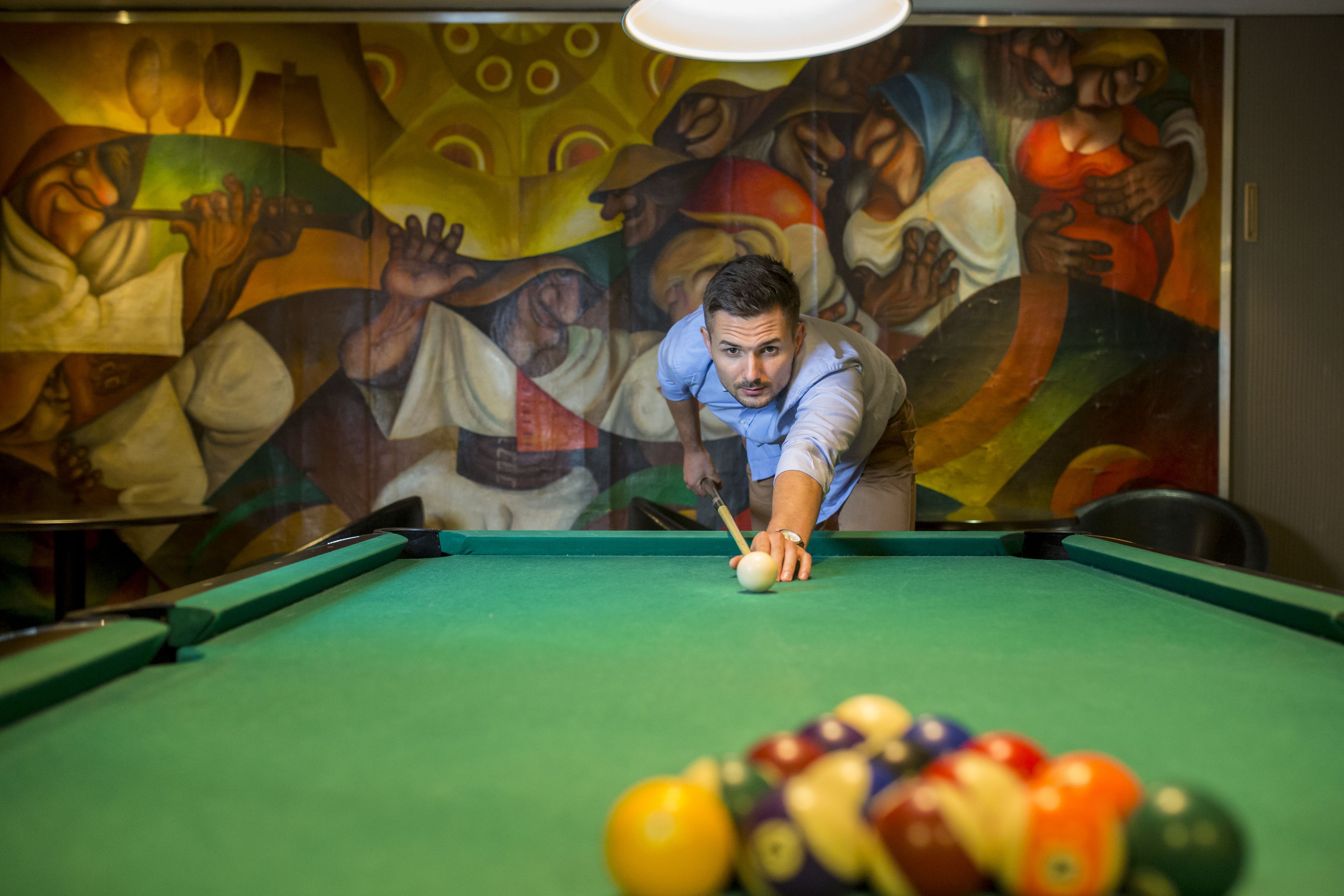 Une table de billard avec une personne qui joue, une fresque colorée en arrière-plan et un tapis vert.