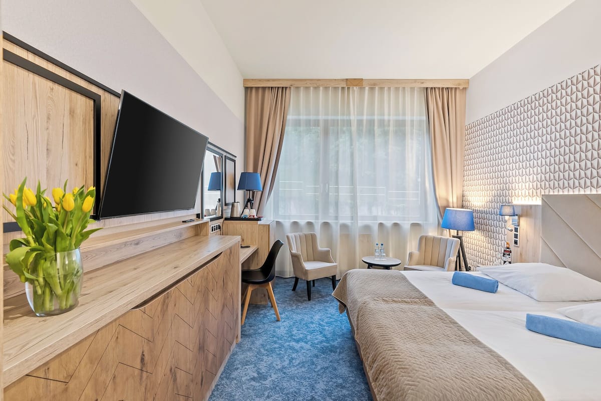 Ein Hotelzimmer mit Holztisch, Bett, Stuhl, Nachttisch und Fernseher.