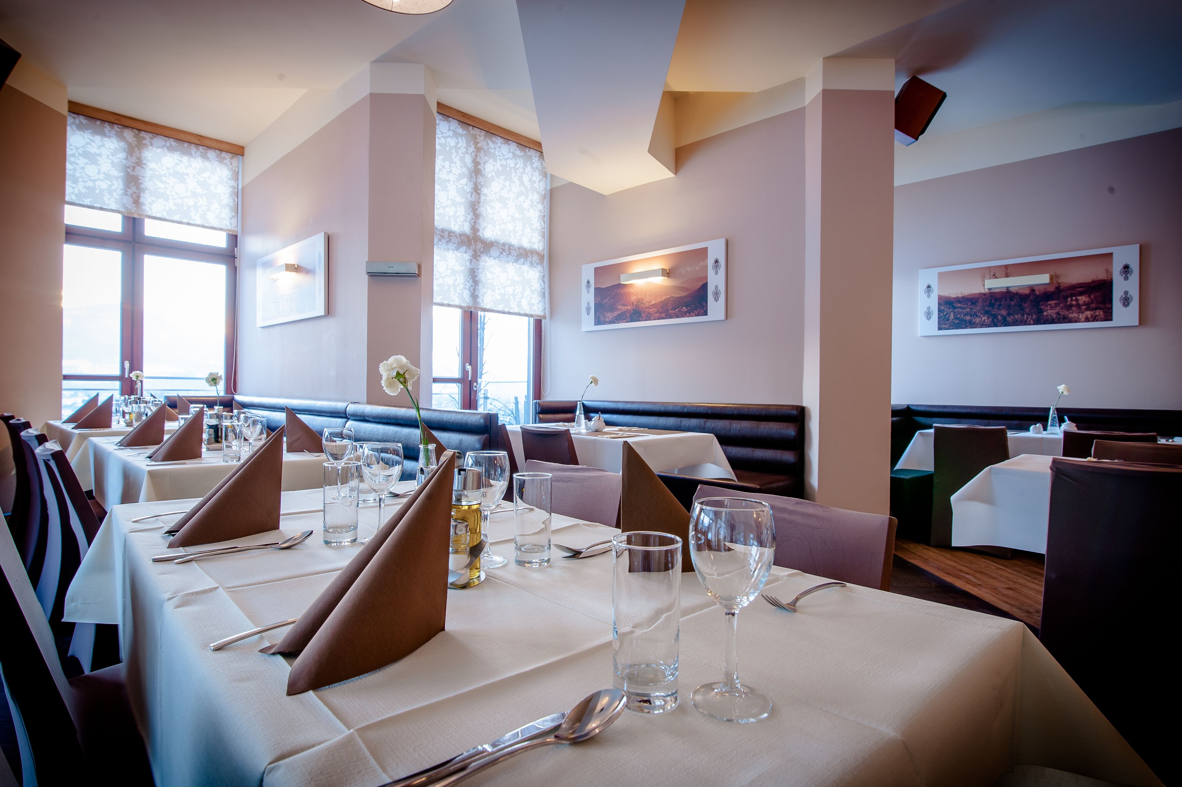 Un restaurante con mesas preparadas para comer, ventanas amplias y obras de arte en las paredes.