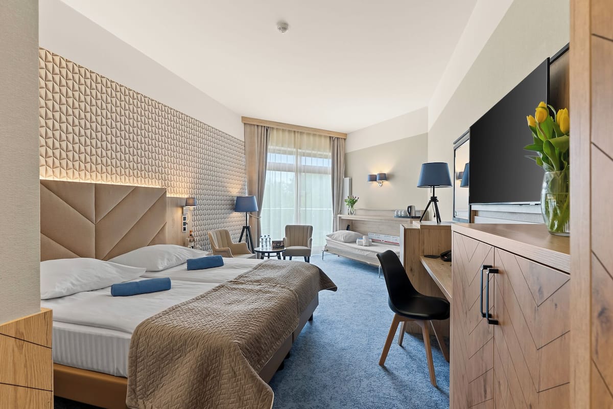Ein Hotelzimmer mit einem großen Bett, einem Schreibtisch, einem Stuhl, einem Fernseher und einer Wand mit geometrischem Muster.