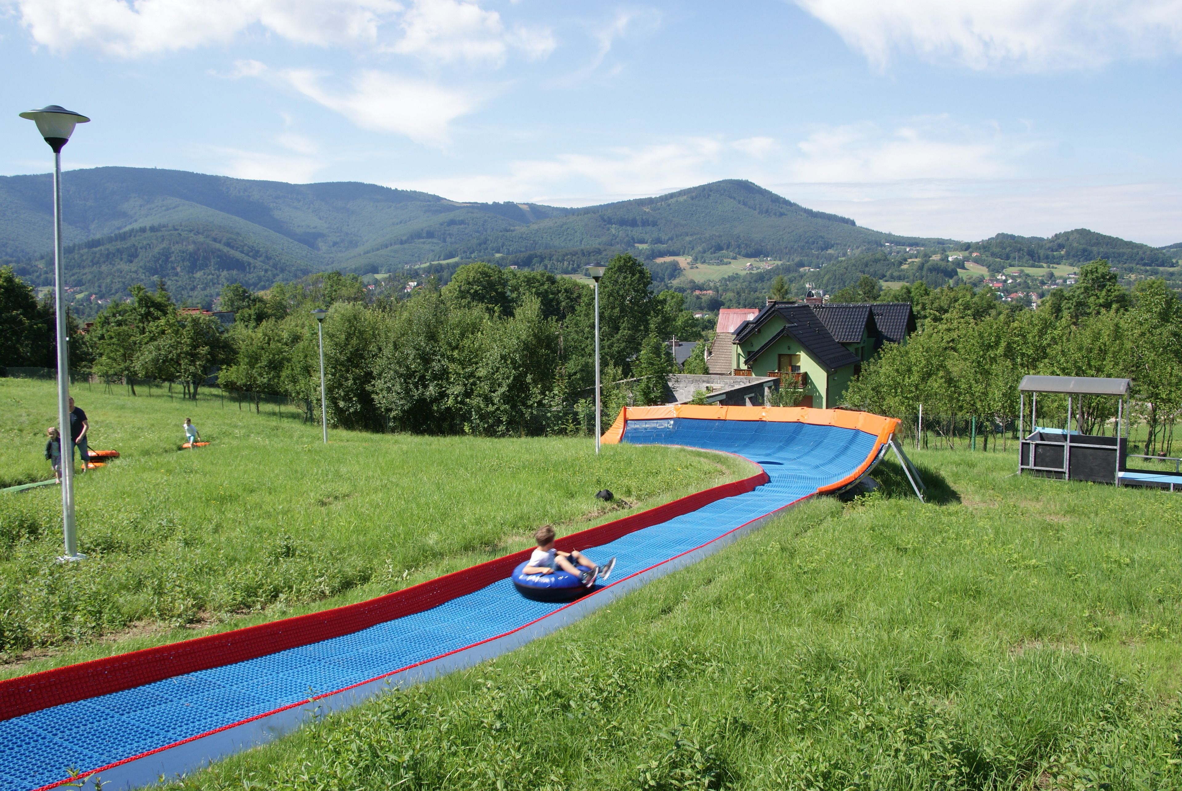 A water slide in a park with a view of green hills and houses in the background.