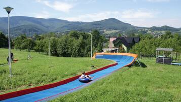A water slide in a park with a view of green hills and houses in the background.