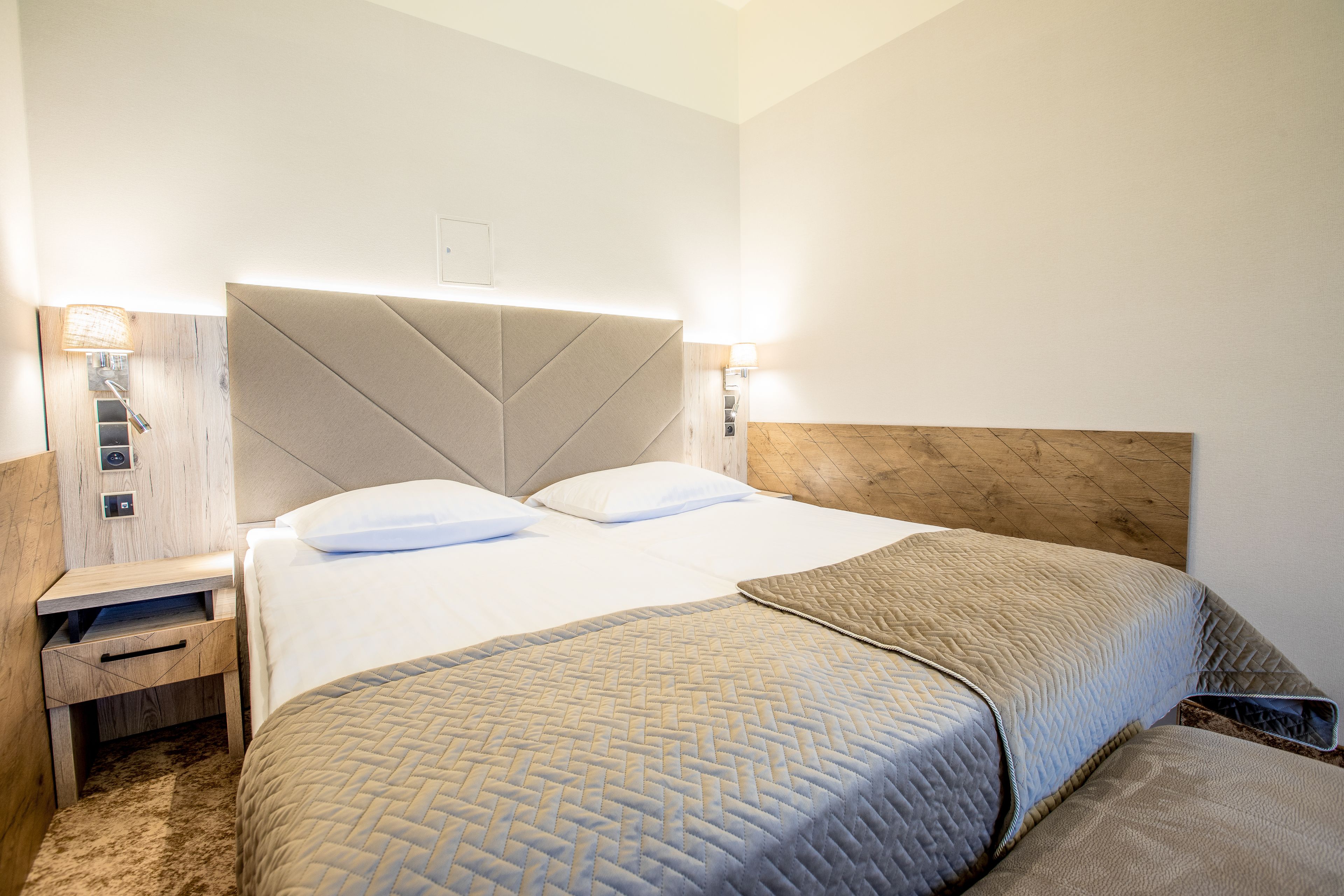 A hotel room with a large bed, a nightstand, and two wall-mounted lamps.