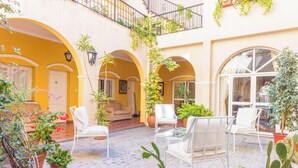 Une cour avec des chaises blanches, des plantes en pot et un sol carrelé.