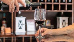Une personne verse du vin dans un verre au comptoir d’un bar, avec une étagère à bouteilles en arrière-plan.
