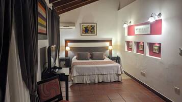 A hotel room with a bed, bedside tables, a desk with a chair, a TV, and a wall with framed pictures.