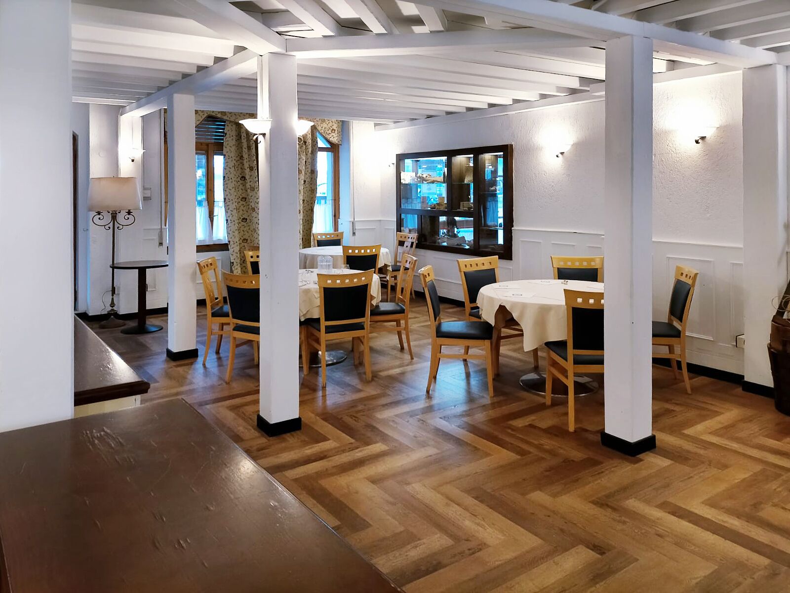 Zona pranzo con tavoli e sedie di legno, pareti bianche e pavimento in legno.