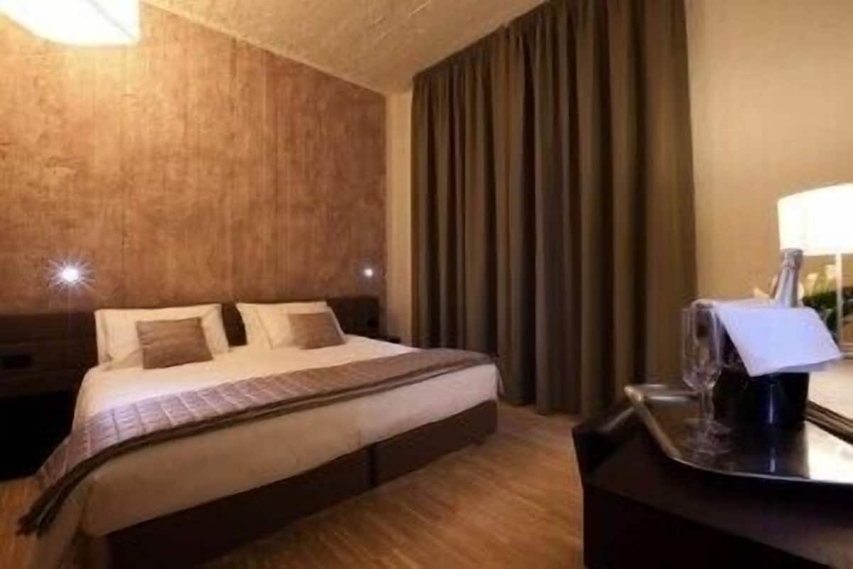A hotel room with a large bed, a nightstand, a lamp, and a curtain.