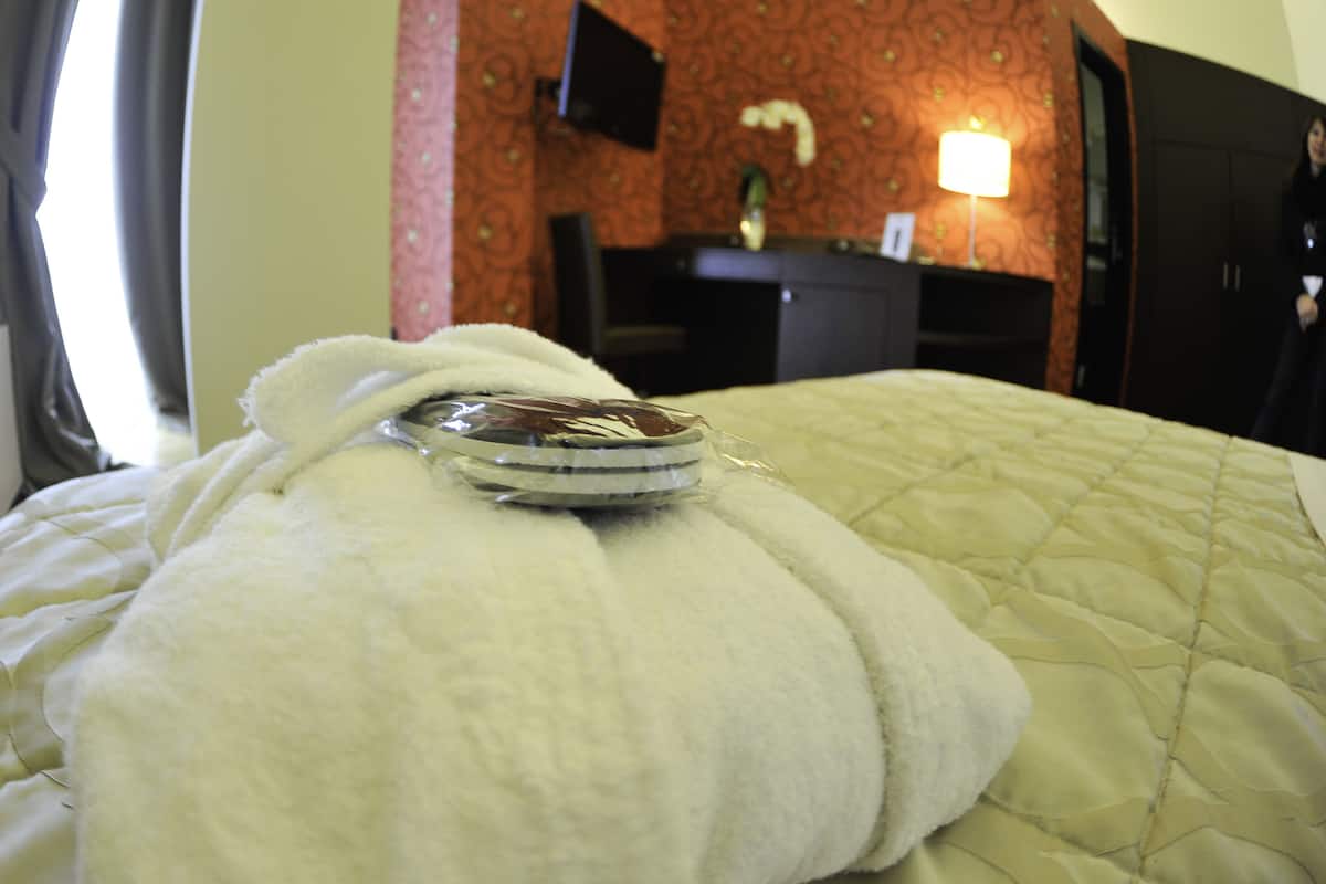 A hotel room with a bed, a robe, and a bedside table with a lamp.