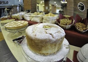 Una mesa de buffet con diversos postres, incluyendo pasteles y productos de repostería, exhibidos sobre un soporte de vidrio.