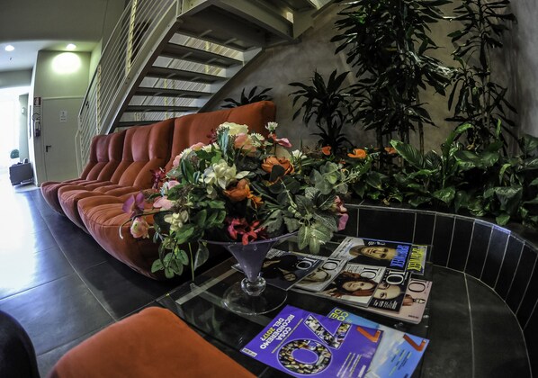 Zona de recepción con sofá, un jarrón de flores, revistas y una escalera.