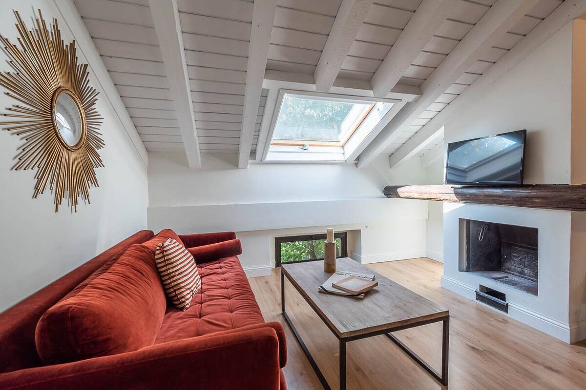 Een loft-woonkamer met een rode bank, een houten salontafel, een open haard, een televisie en een dakraam.