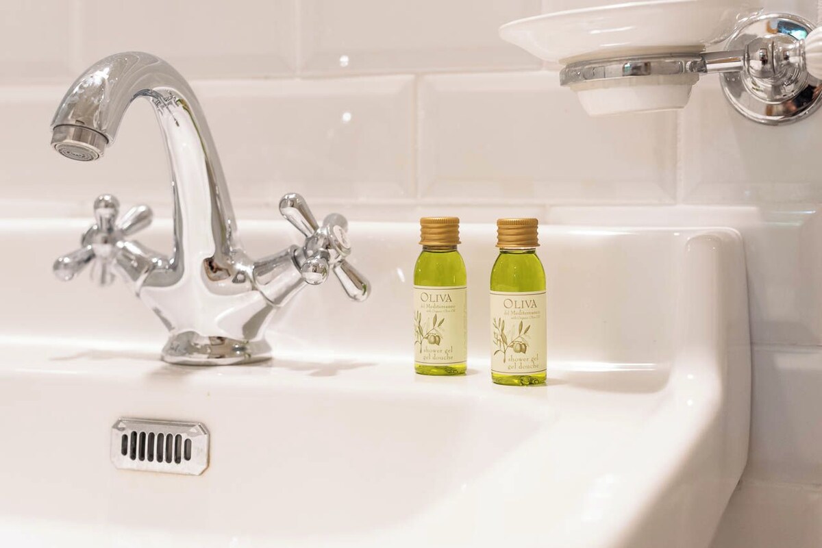 Un lavabo de salle de bain avec un robinet chromé et deux bouteilles d’huile d’olive.