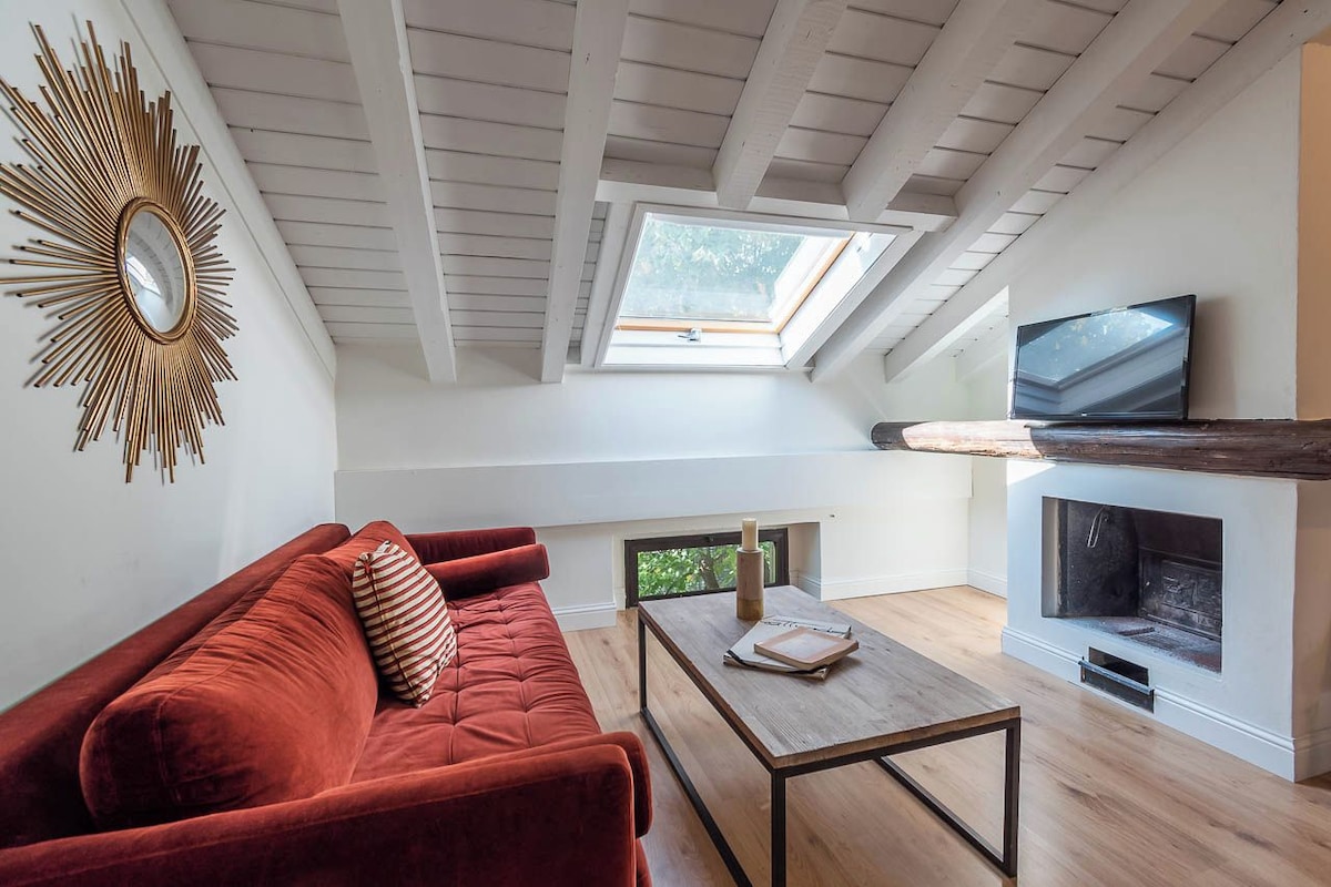 A loft-style living room with a red sofa, a wooden coffee table, a fireplace, a TV, and a skylight.