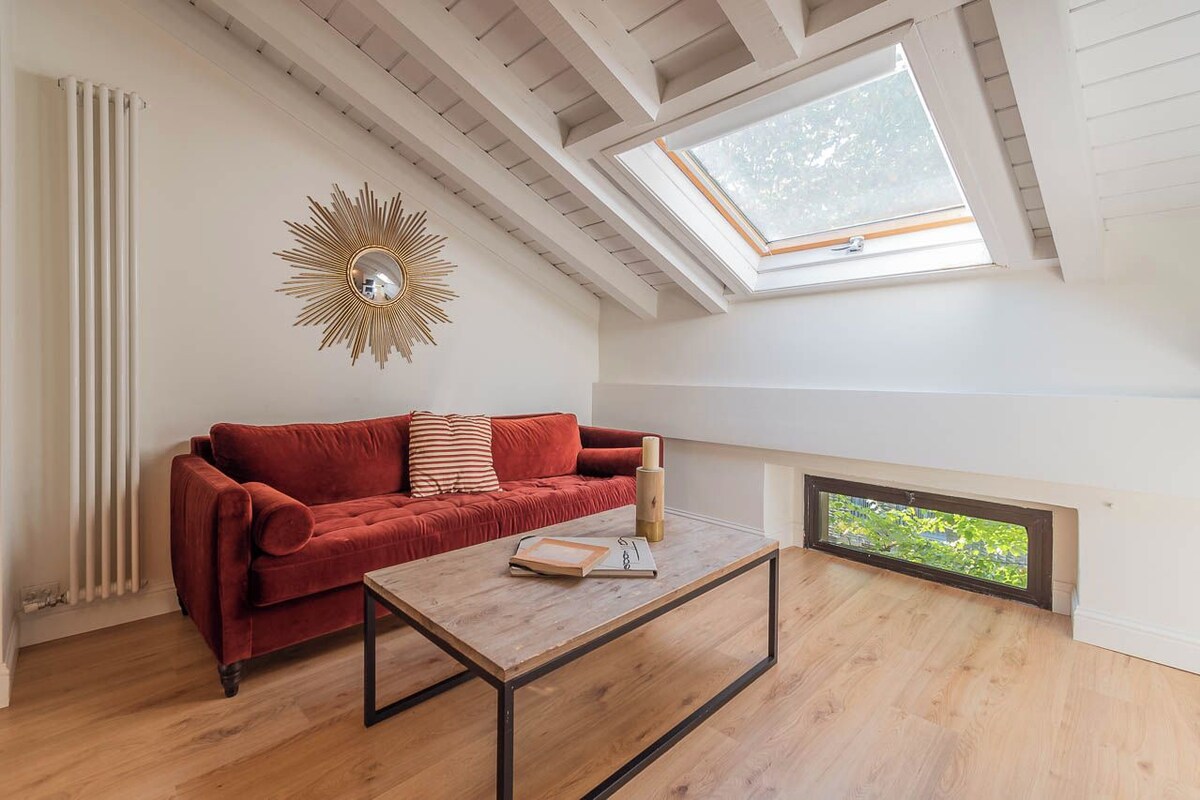 Une pièce avec un canapé rouge, une table basse en bois, un miroir en forme de soleil et une lucarne.