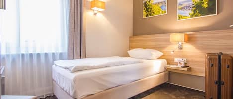 Une chambre d’hôtel avec un lit, une table de chevet, une valise et deux lampes fixées au mur.