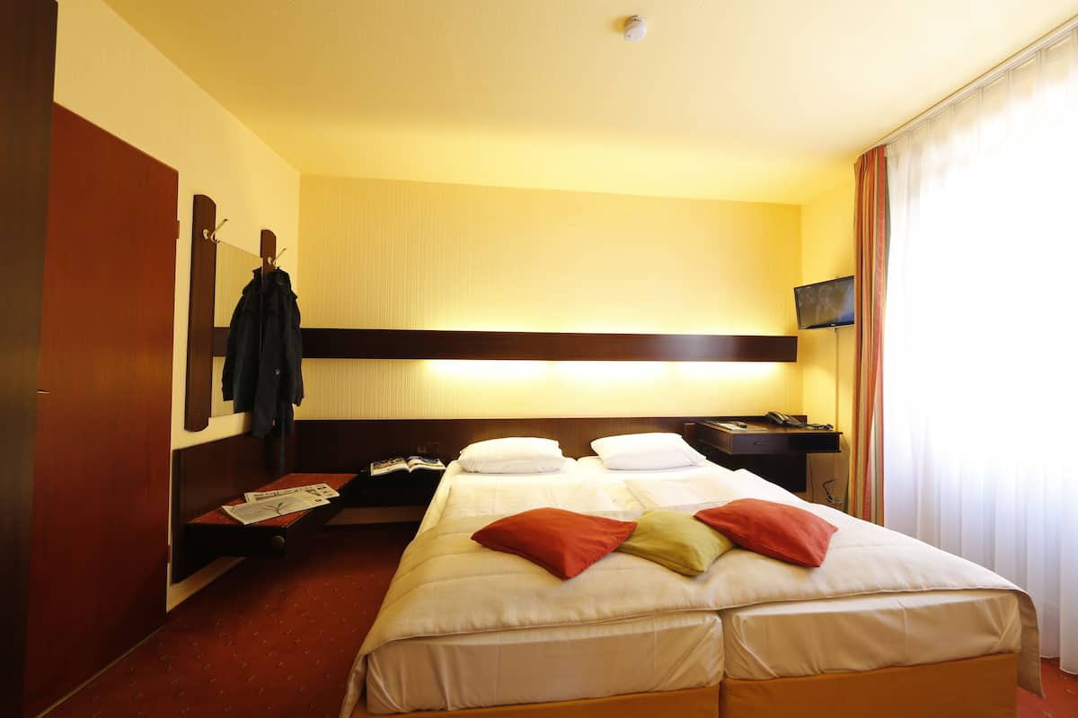 A hotel room with a large bed, a desk with a computer, a TV, and a coat rack.
