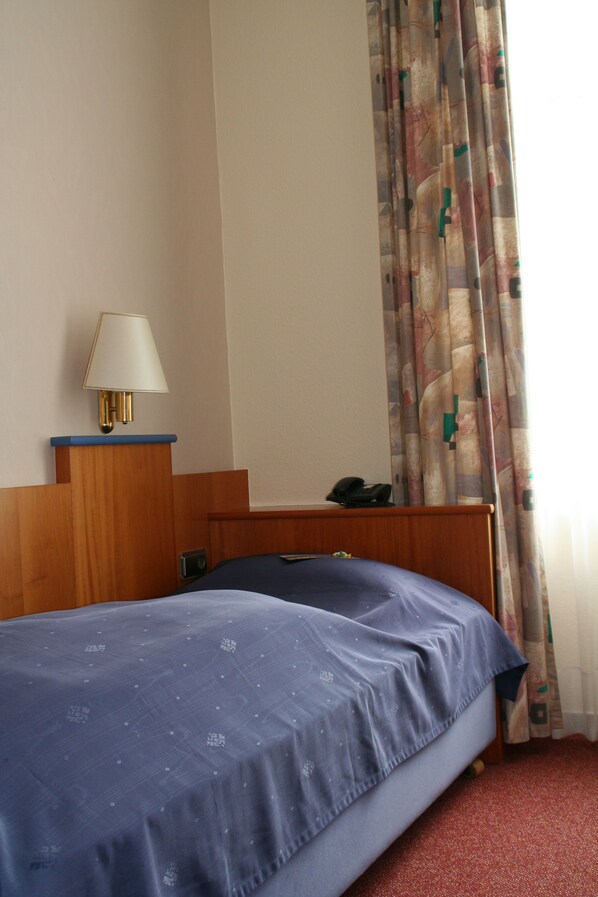 Una habitación de hotel con una cama, una mesita de noche con lámpara, teléfono y cortina.