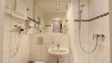 Un baño pequeño y limpio con lavamanos, espejo, ducha y toallero.