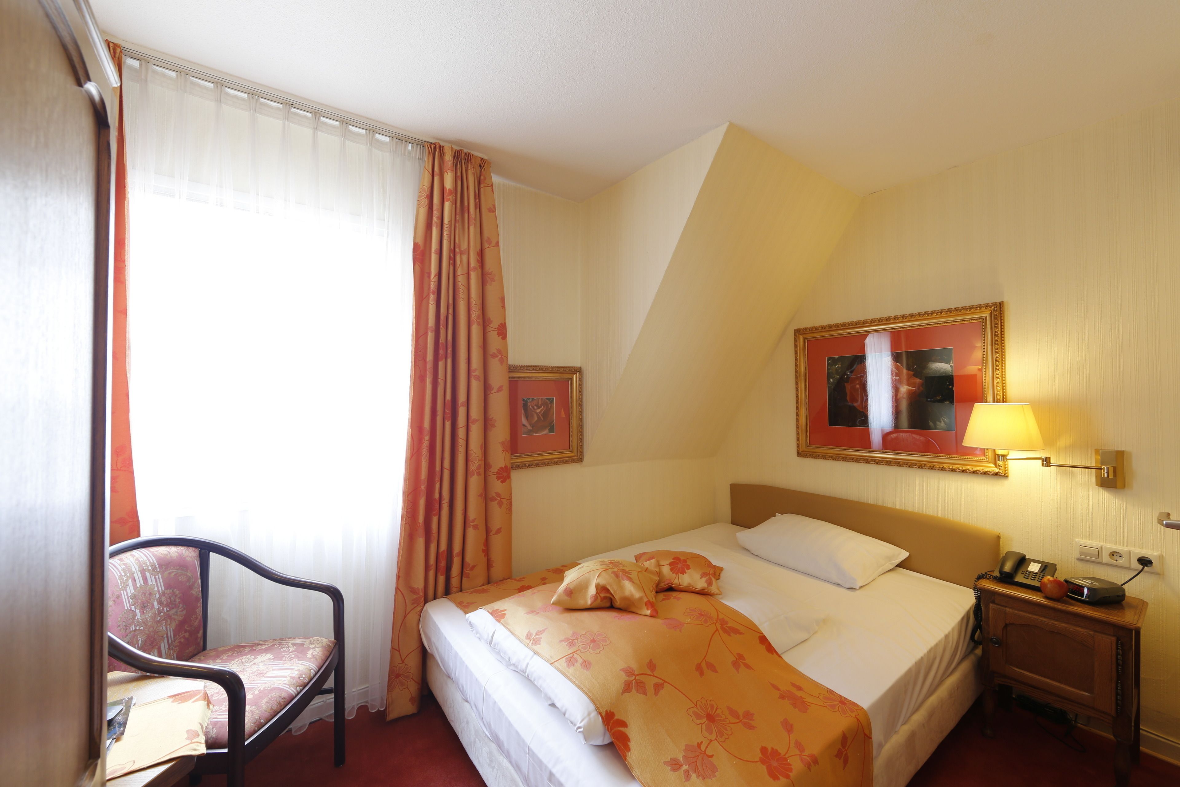 Une chambre d’hôtel avec un lit, une chaise, une table de chevet avec une lampe et un tableau encadré au mur.