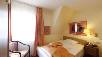 A hotel room with a bed, a chair, a nightstand with a lamp, and a framed picture on the wall.