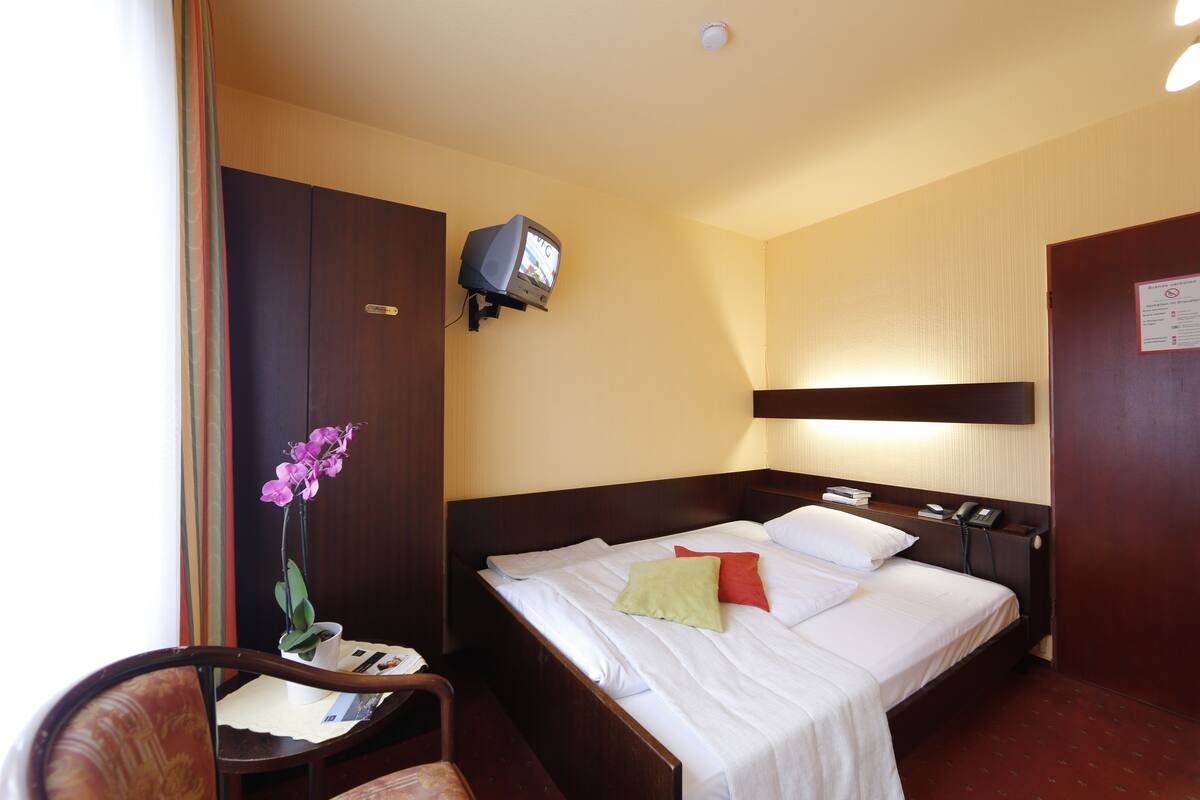 A hotel room with a bed, bedside table, chair, and a small television.