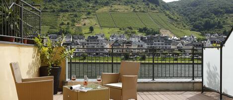 A balcony with wicker furniture, a glass table, and a view of a town and hills.