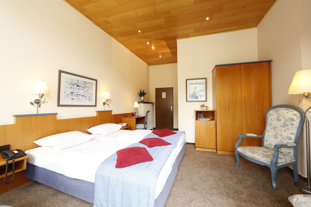 A hotel room with a bed, bedside tables, a chair, a wardrobe, and a desk with a lamp.