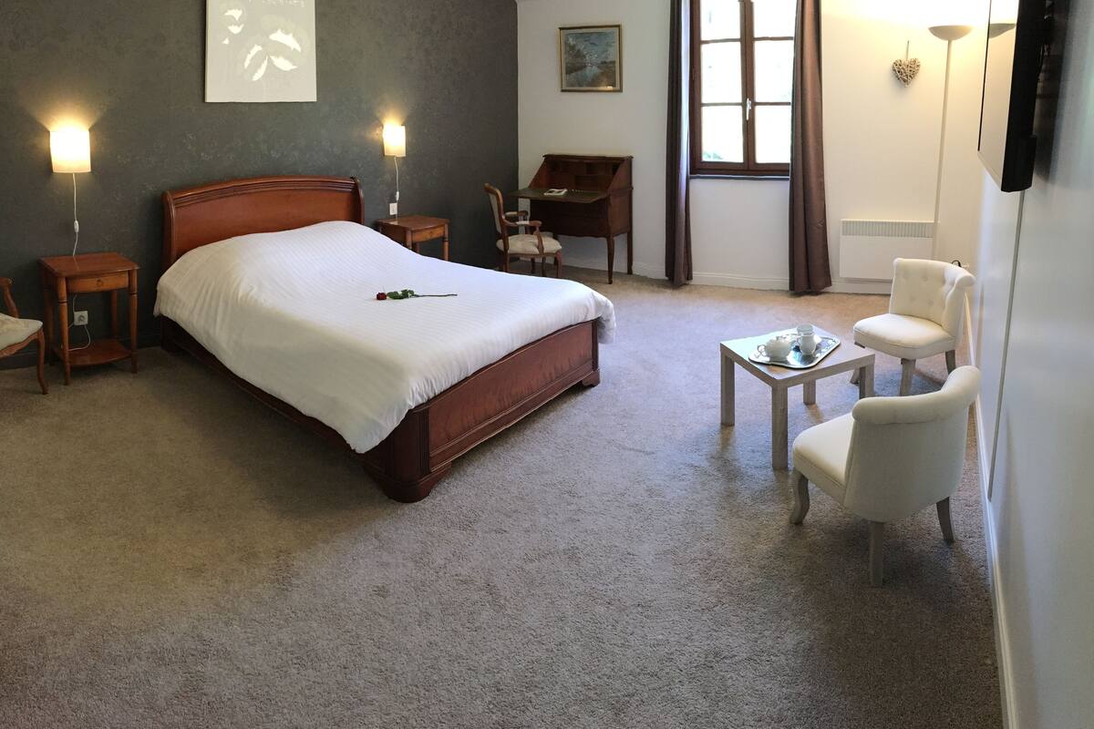 Quarto com cama de madeira, duas mesas de cabeceira, escrivaninha, cadeira e janela com cortinas.