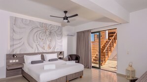Un dormitorio moderno con una cama grande, un ventilador de techo, una mesita de noche, una silla y vista a una escalera de madera.