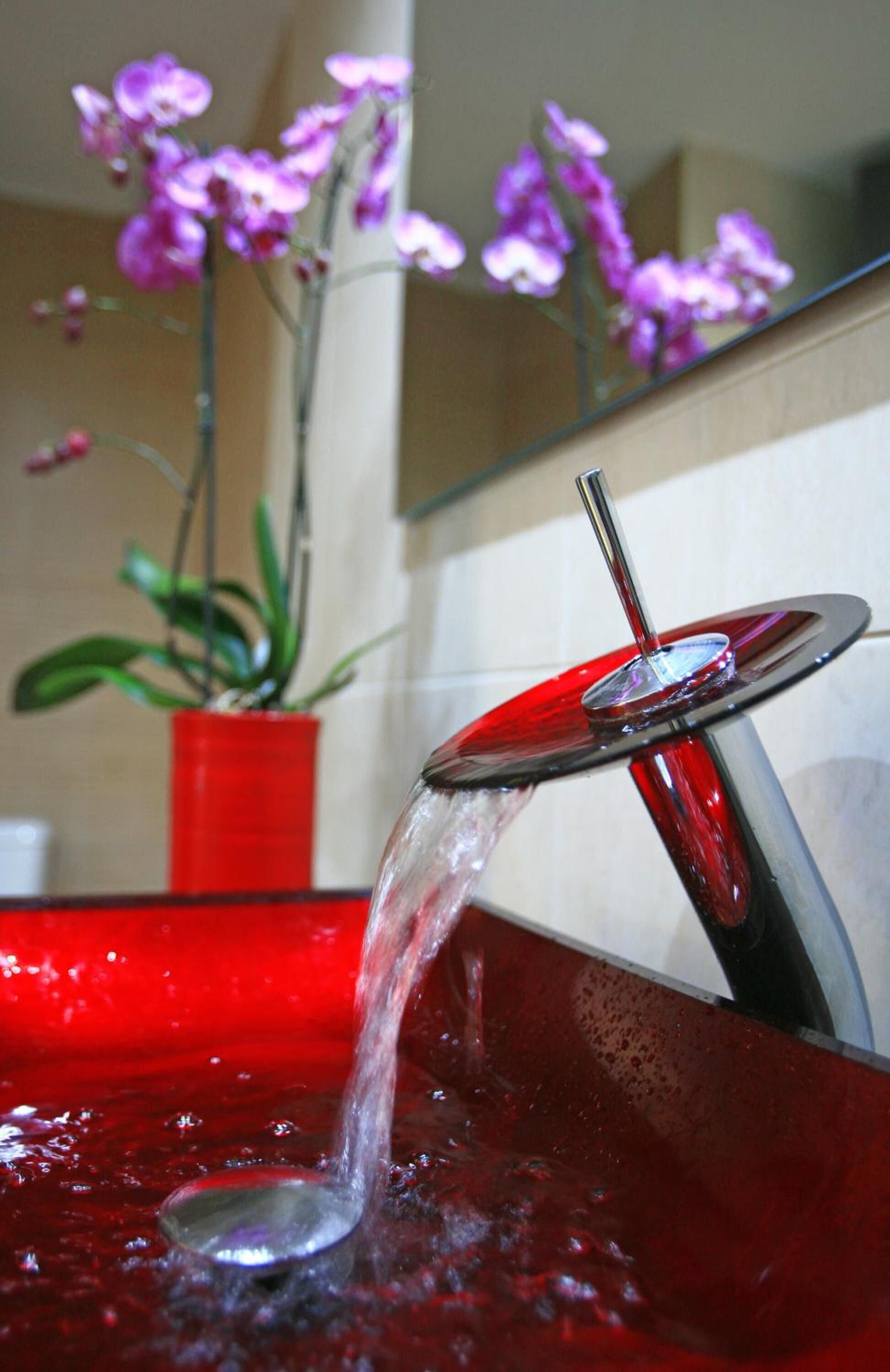 A bathroom with a red sink, a glass water feature, and a potted plant with purple flowers.