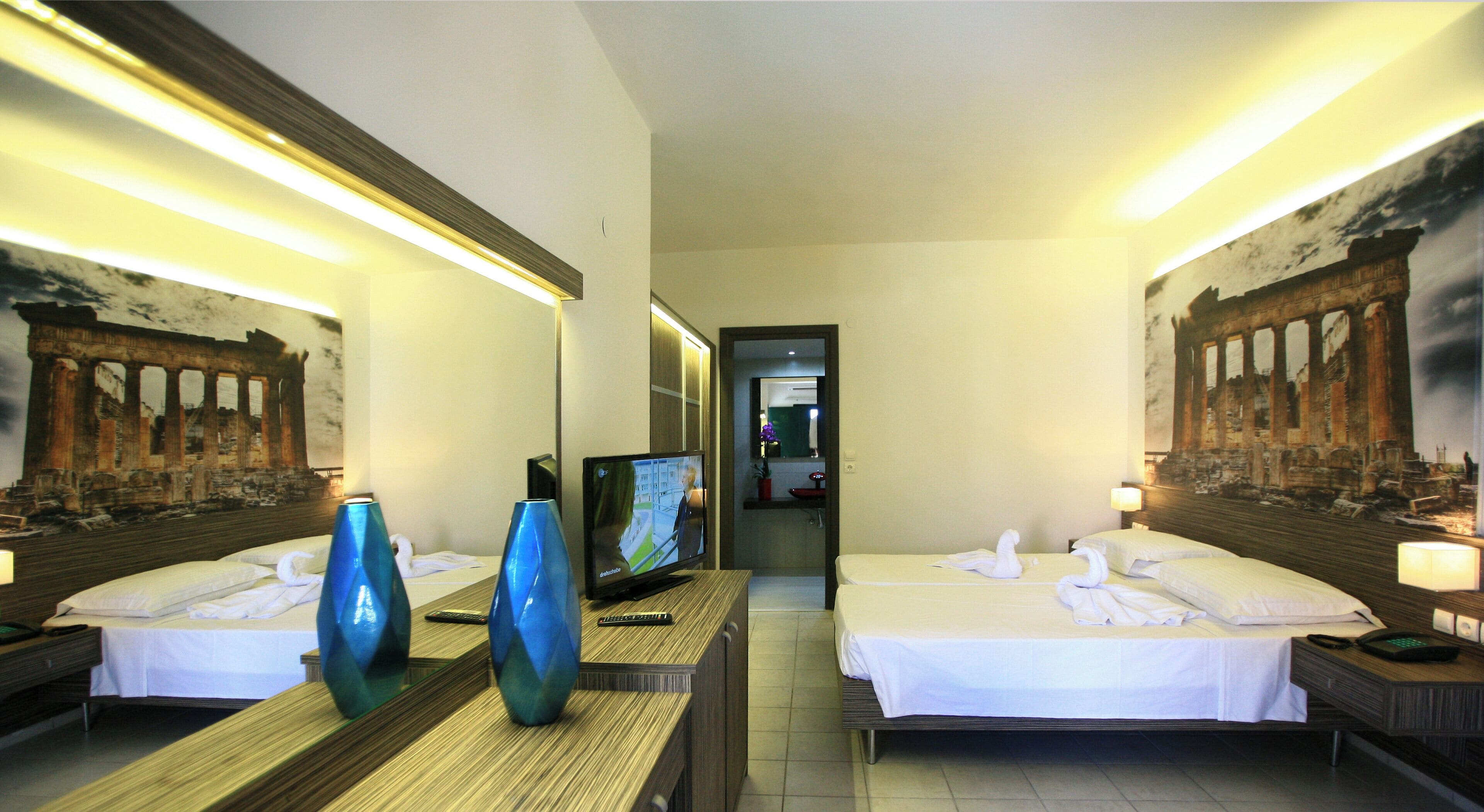 Een hotelkamer met twee bedden, een televisie en kunstwerken die oude ruïnes voorstellen.