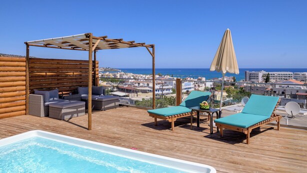 Área de piscina en la azotea con sillones de descanso, una pérgola y vistas a la ciudad y al mar.
