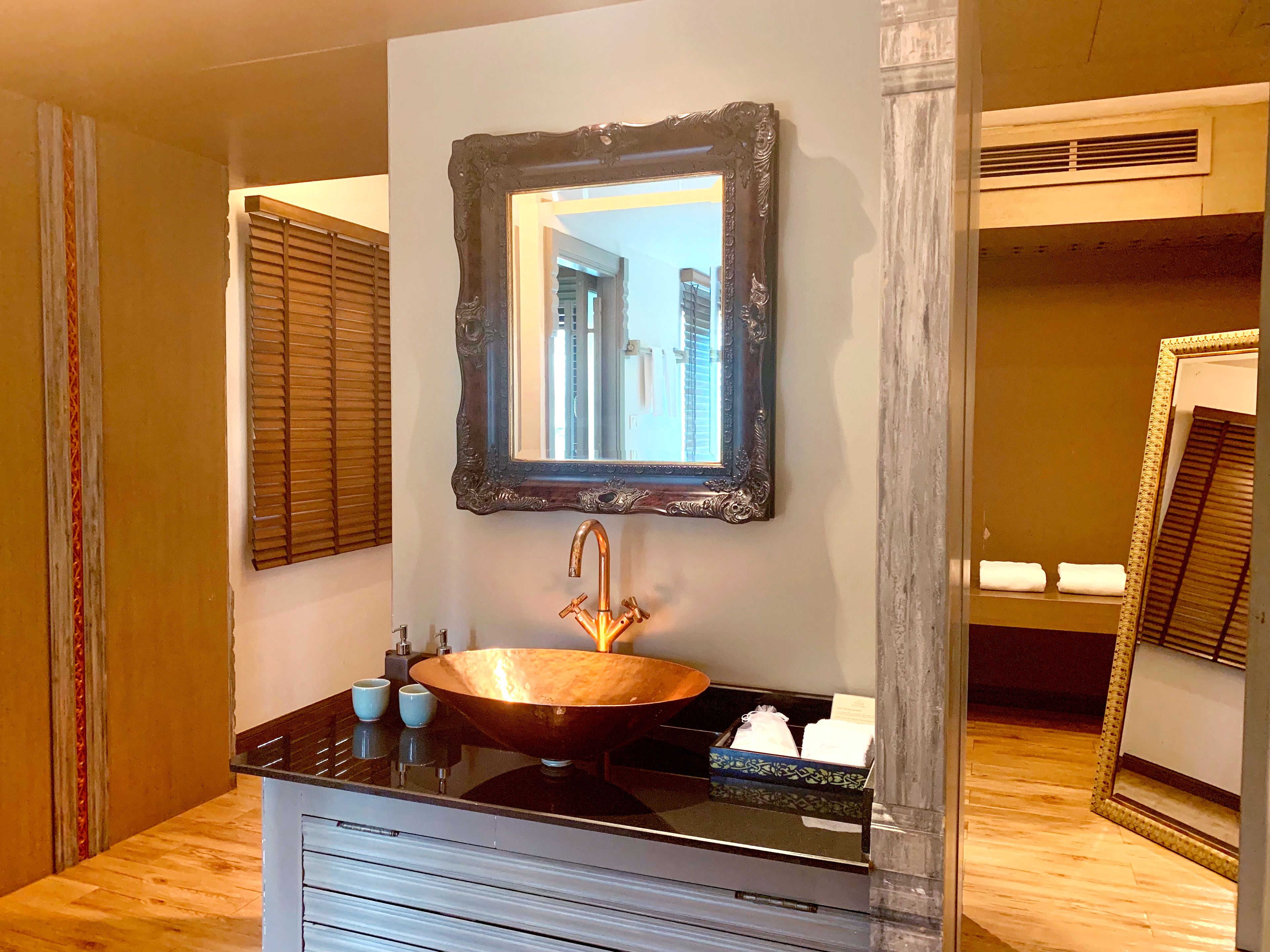 A bathroom with a large mirror, a copper sink, and wooden blinds.
