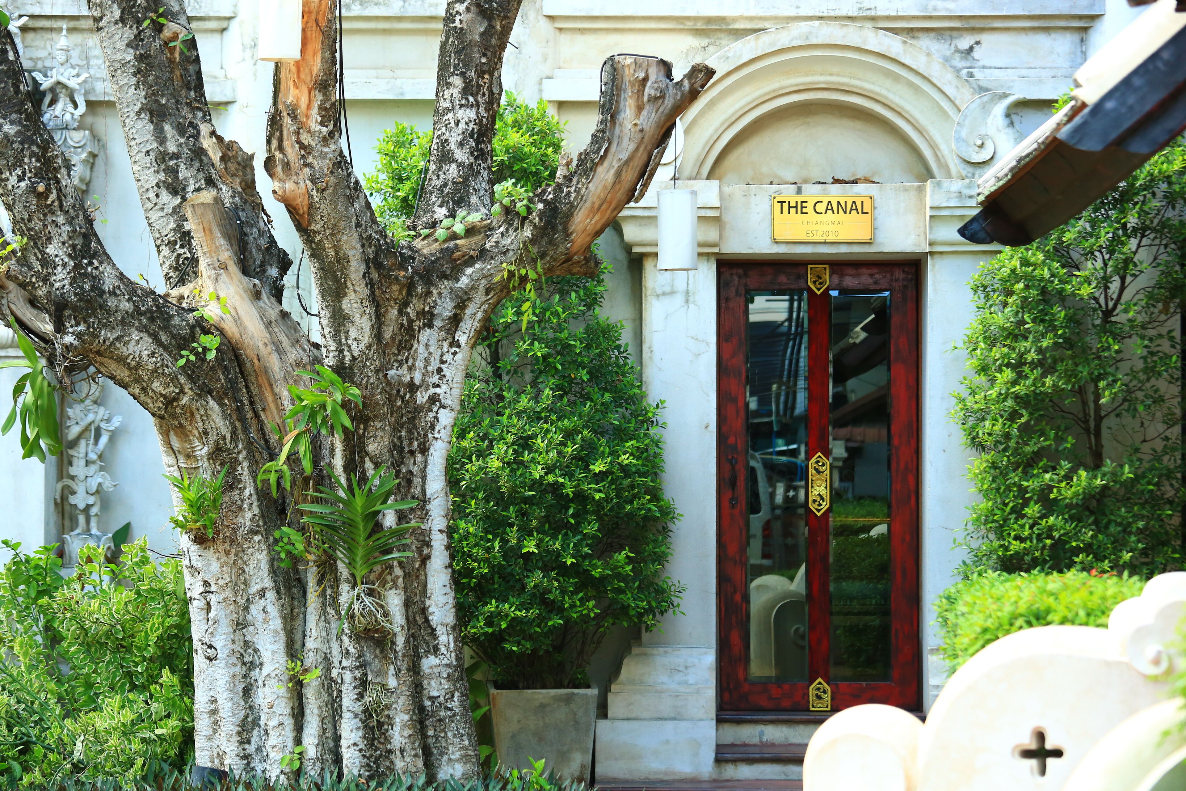 Un edifici amb una porta vermella amb la inscripció 'THE CANAL' i un cartell que indica 'CHIANGMAI EST.2010'.