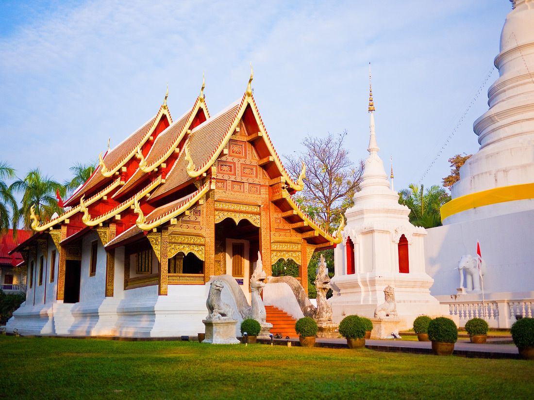 A traditional Thai temple with ornate architecture, including a multi-tiered roof and a prominent white stupa.