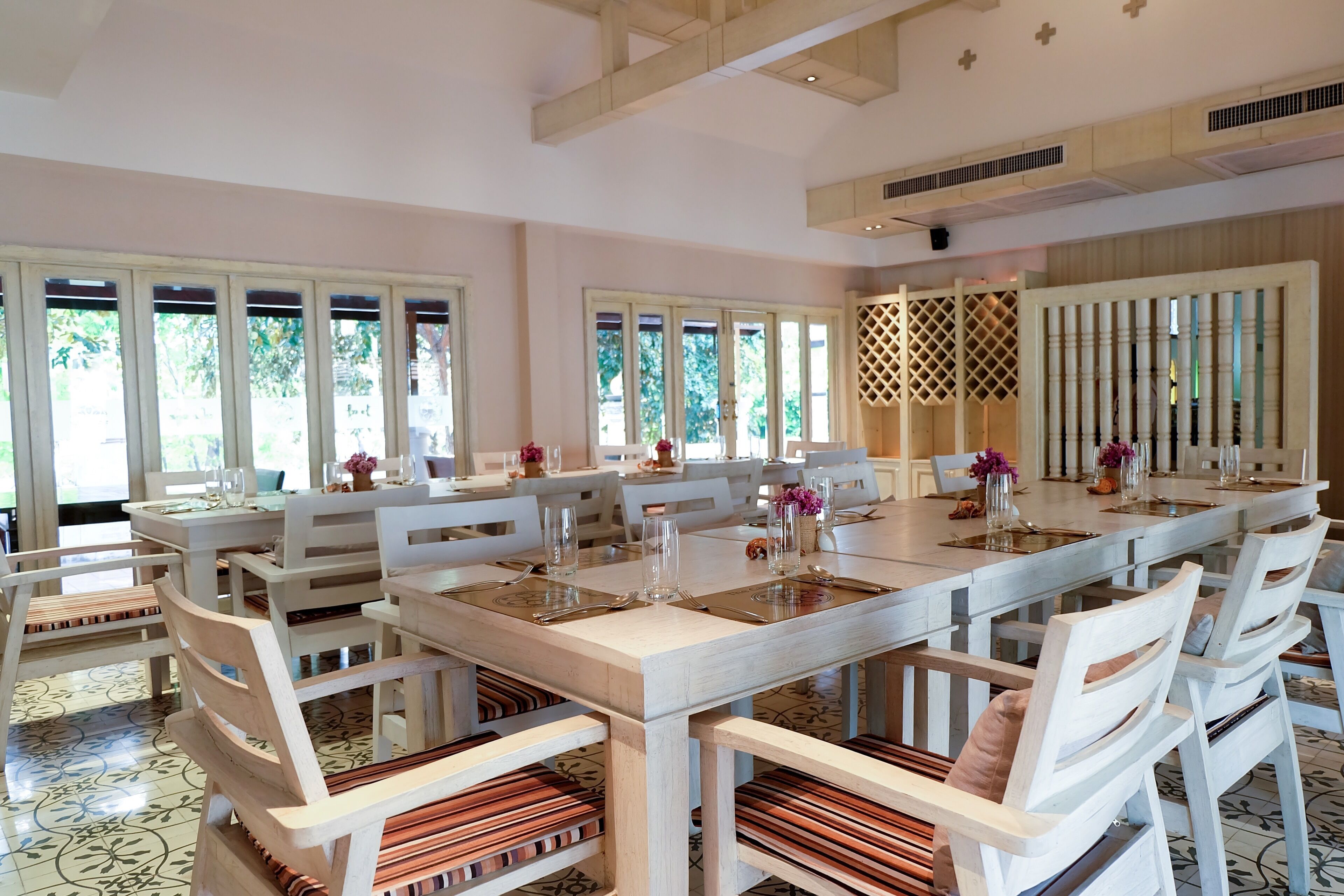 Une salle à manger spacieuse avec une longue table dressée pour accueillir de nombreux convives, entourée de chaises blanches dotées d’assises rembourrées.