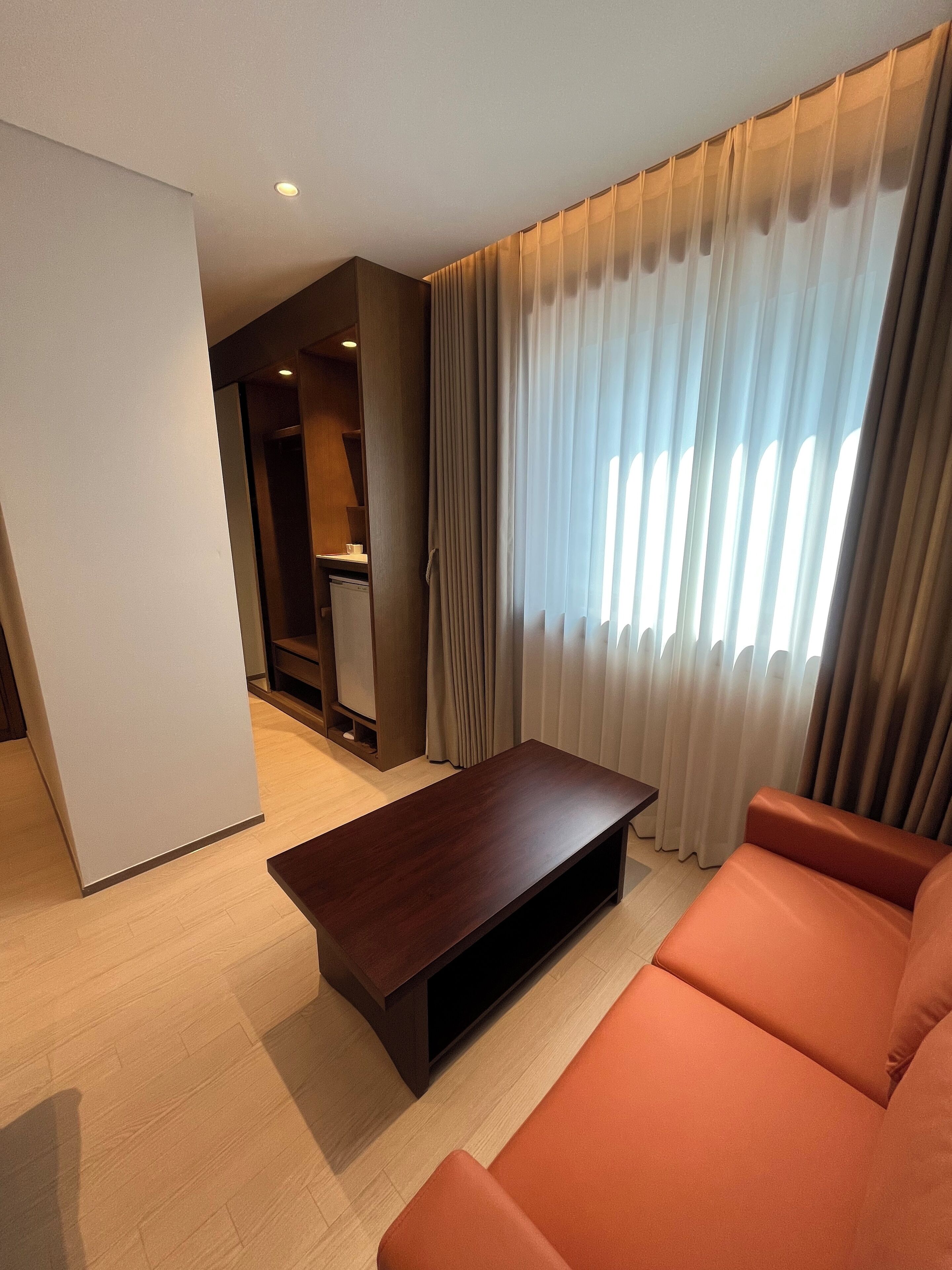 A modern living room with a dark wooden coffee table, a brown sofa, and a view through sheer curtains to a balcony.