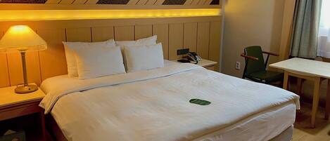 Una habitación de hotel con una cama, una mesita de noche con lámpara, una silla, una pequeña mesa y un teléfono en el buró.